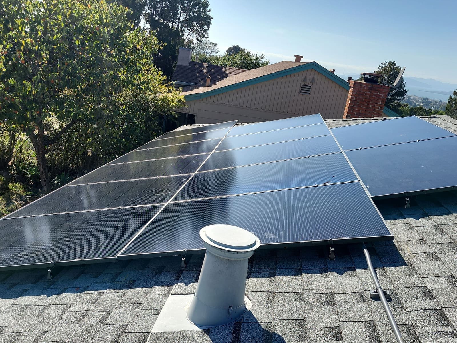 Solar panels on a hillside roof with a distant bay view behind