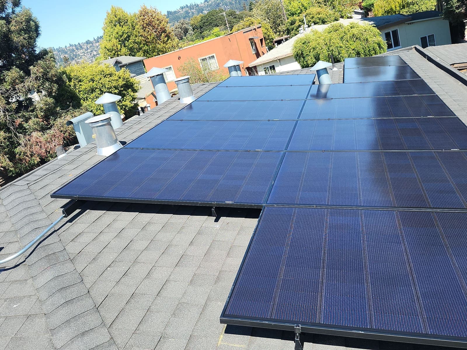 Solar panels laid across a low-slope roof in a hillside neighbourhood